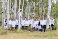 a group of people in white coats posing for a photo in a forest